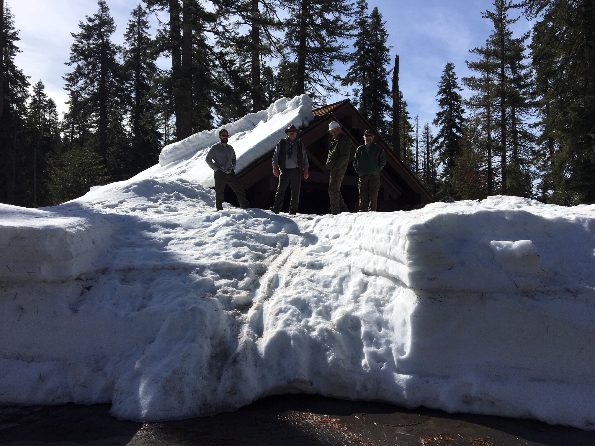 Rangers stand on the snowpack at the Sherman Tree comfort station