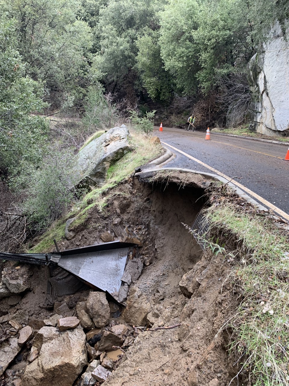 A road on a steep drop off shows the ground beneath the road eroding.