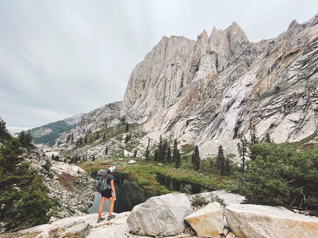 Backpacker looks up at craggy mountains