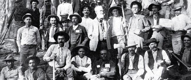 A group of people from the 1900s standing in front of a sequoia tree.