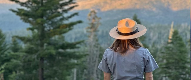 A ranger looks out towards amountain range during sunset.