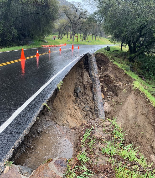 A section of Generals Highway with stone guard rails washed off the road edge and soil beneath the paved surface clearly undercut