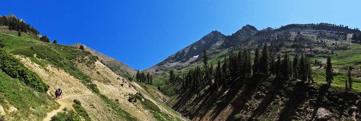 Hikers walk along a trail that climbs to a mountain pass