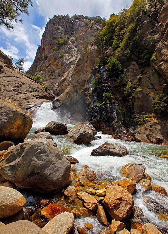 Roaring River Falls full of spring runoff, cascading over red-brown boulders.