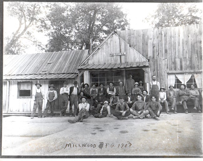 men stand in front of a wood building with a Post Office sign