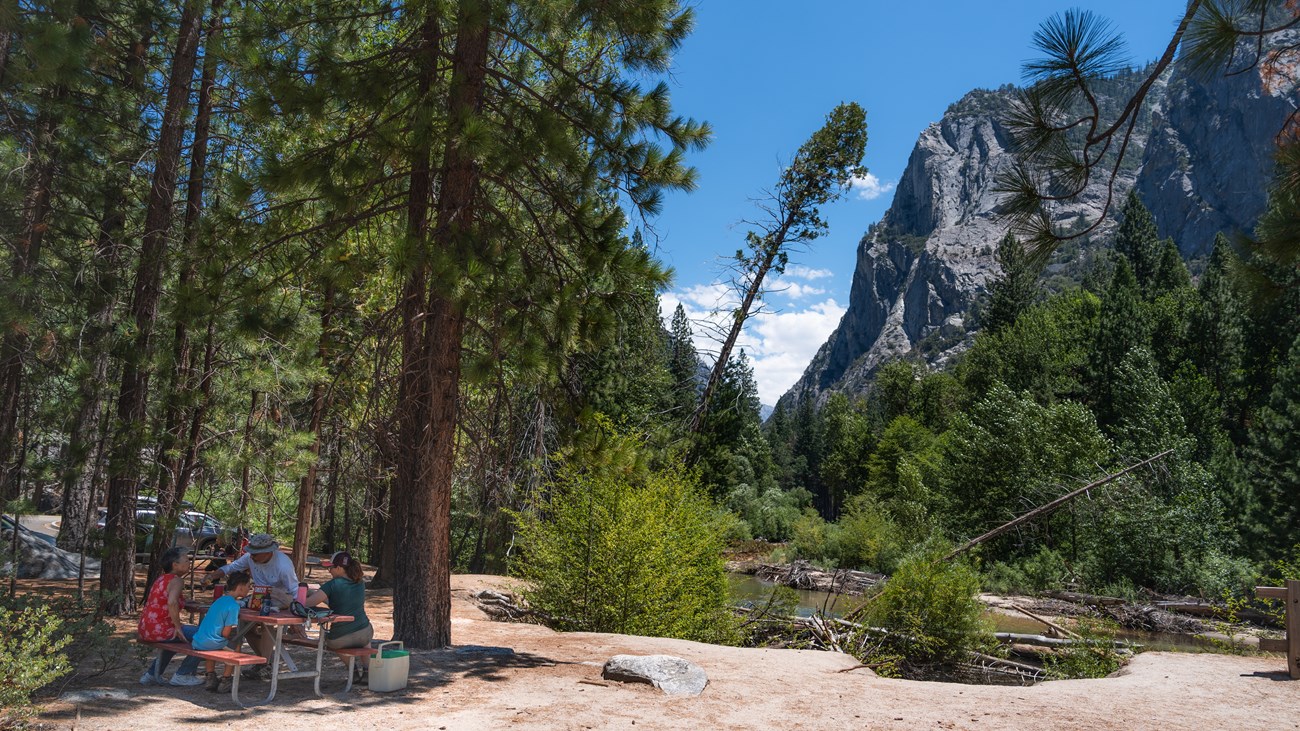 A family sits at a picnic table by the river.