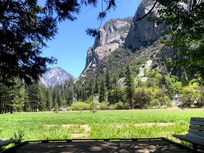 Wood deck overlooking a green meadow with soaring granite cliffs in the background.