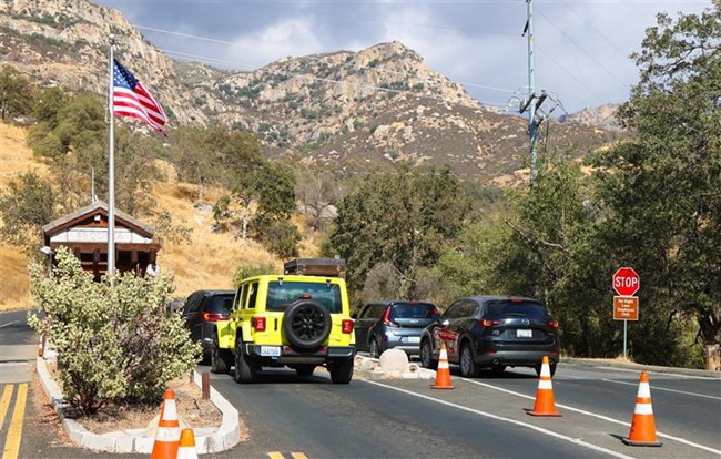 A group of cars lined up in front of a park entrance station in the foothills.