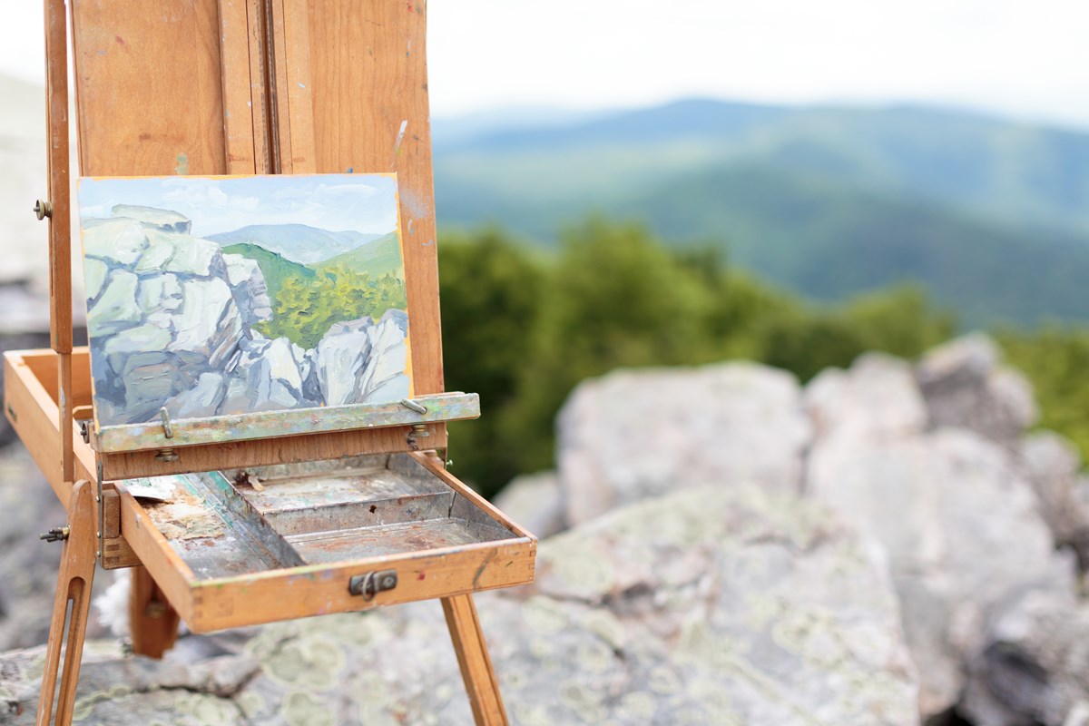 An artist's plein air painting supplies and easel on a rocky overlook.