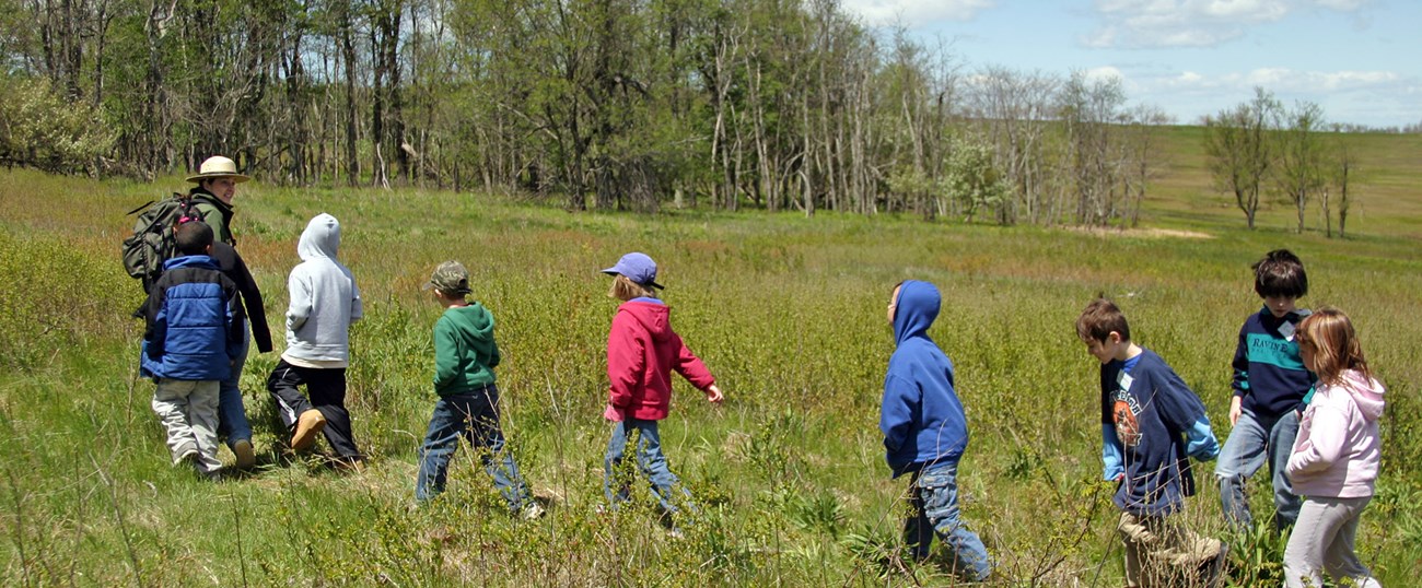 A Ranger leading a group of students through a meadow.