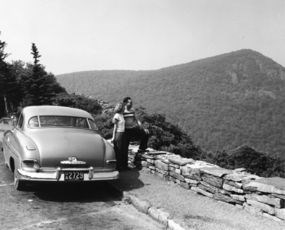 Old car and couple on drive overlook.