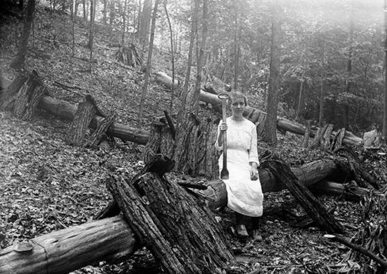 A young girl posing against a fallen tree with a tool called a "spud."