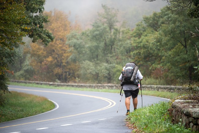 A hiker with backpacking gear walking along a curve of Skyline Drive.