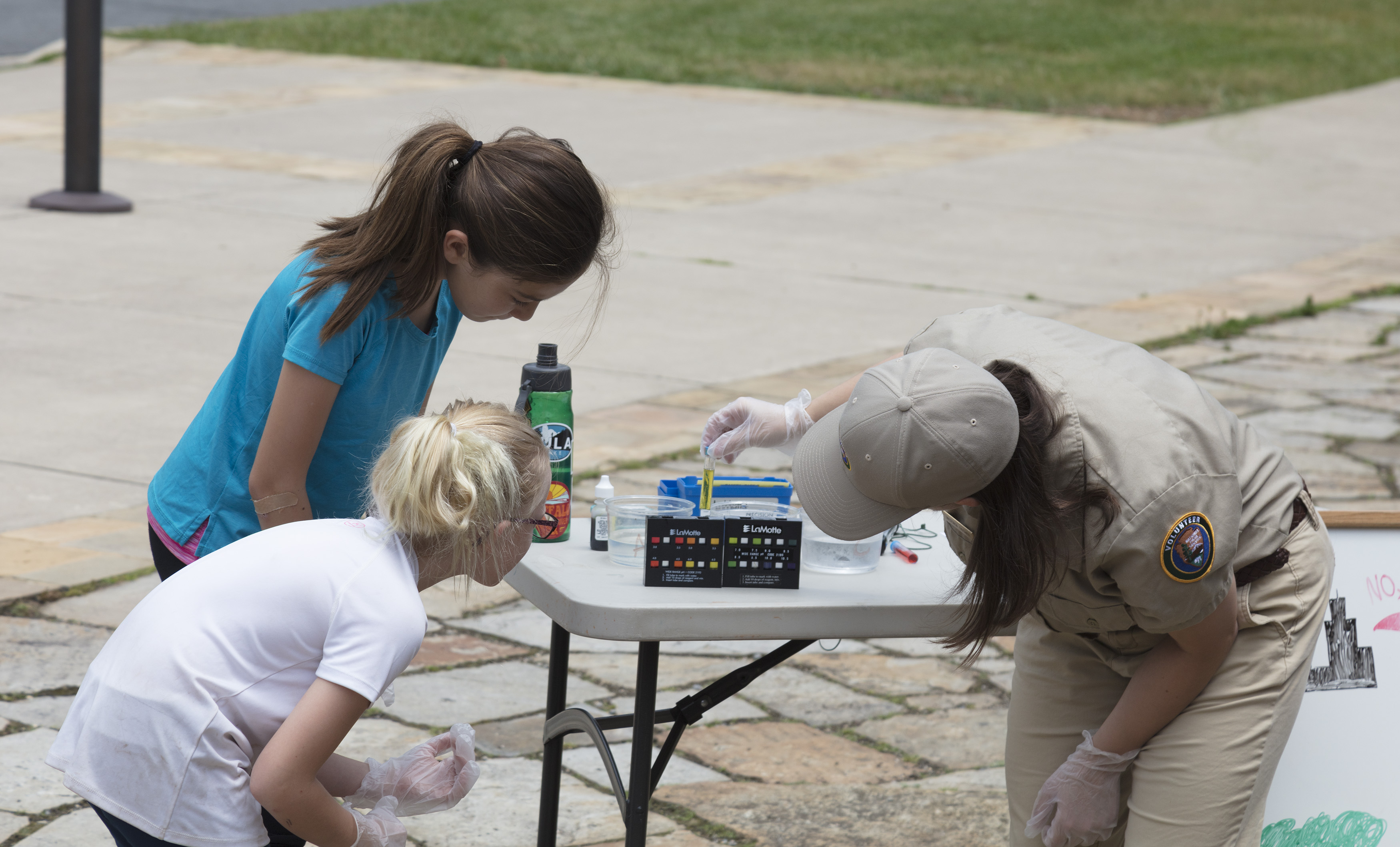 A volunteer and two girls look at water quality testing instruments.