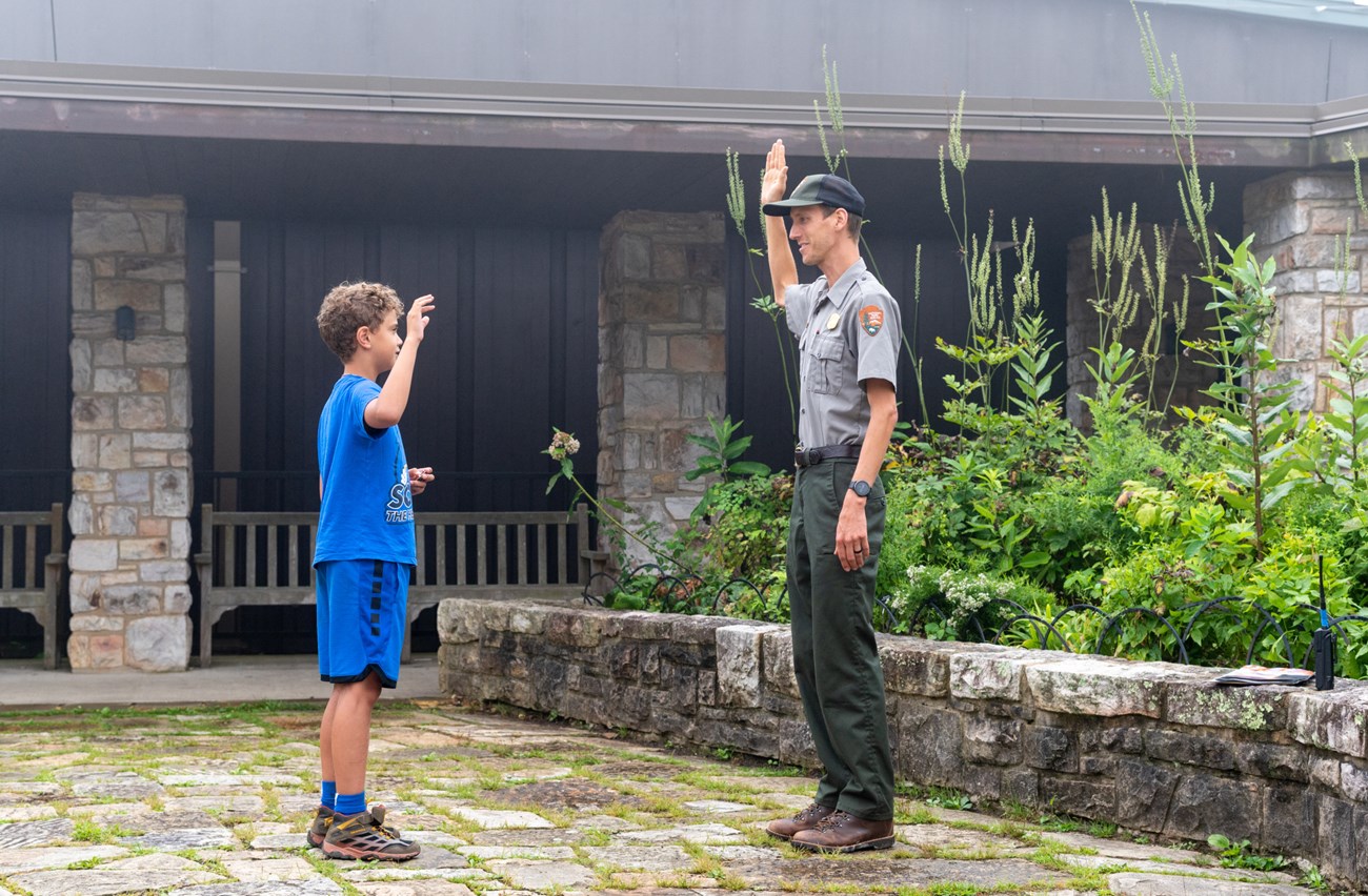 A ranger and child both with right hands raised for a Junior Ranger swearing in.