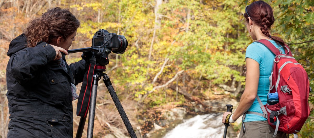 A videographer films a hiker posing for the camera in front of a landscape of fall color. A videographer films a hiker posing for the camera in front of a landscape of fall color.