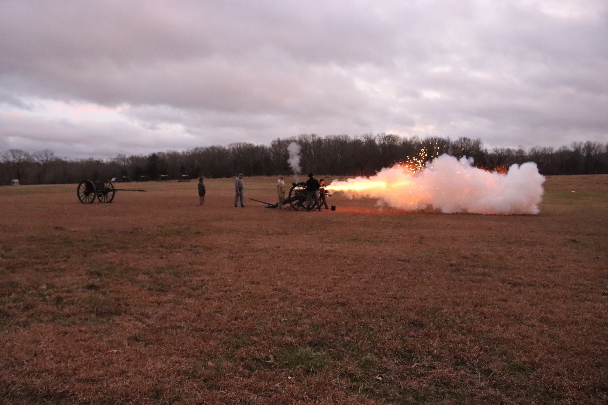 Sparks and smoke are propelled from a cannon muzzle with volunteer cannoneers standing nearby.