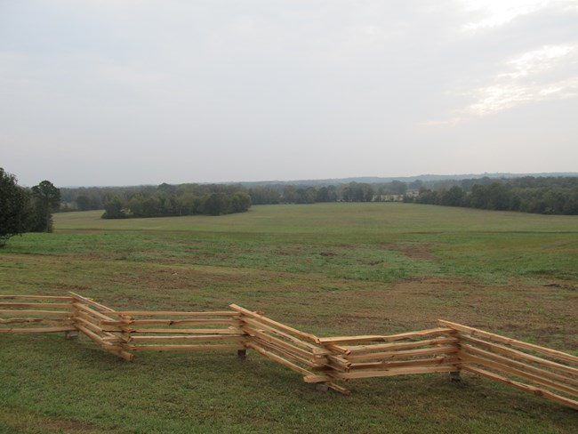 Image of an open field with a split rail fence in foreground