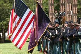 A Union Civil War unit with flags stands in front of a brick platform.