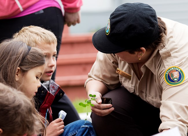 Volunteer kneels with children in heritage garden.