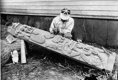 Historical photograph of a man carving a totem pole