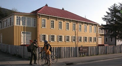 Wood pale fence around a large two-story building with a tin roof and many windows