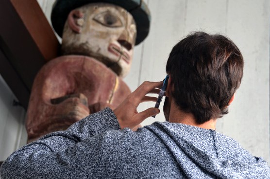 A man looking at a totem pole while listening to his cell phone.