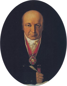 Photo of a painting that consists of a portrait of a man who is wearing a medal and is sitting at a desk.
