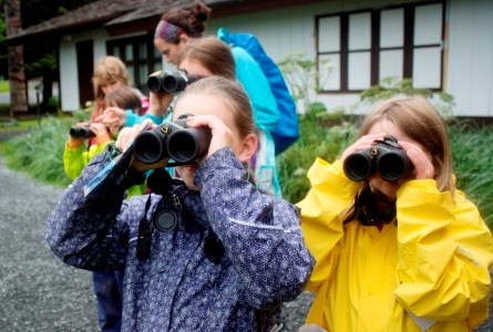 A group of kids in rain jackets looking through binoculars.