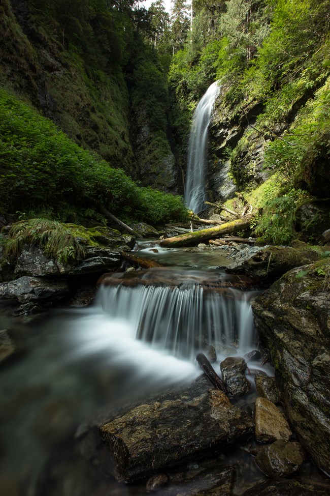 A closed canyon with a large waterfall, lush greenery.