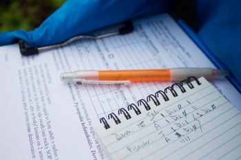 Close-up of a clipboard holding data sheets, a small notebook and a pen.