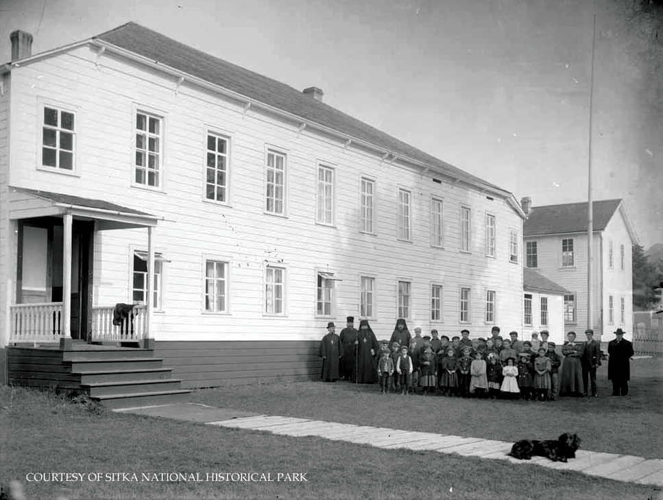 Long two-story building with a group of priests and children on a lawn