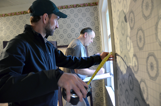 Photo of two engineers measuring and taking notes of room dimensions and attributes in the Russian Bishop's House.