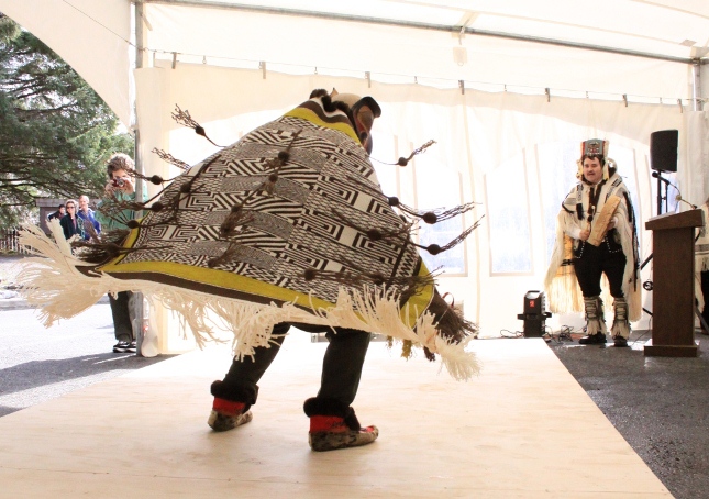 Photo of people viewing a traditional dancer demonstrating an ornate, textile robe.