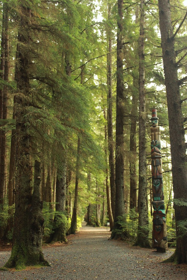 Trail lined with trees, with a totem pole on the right
