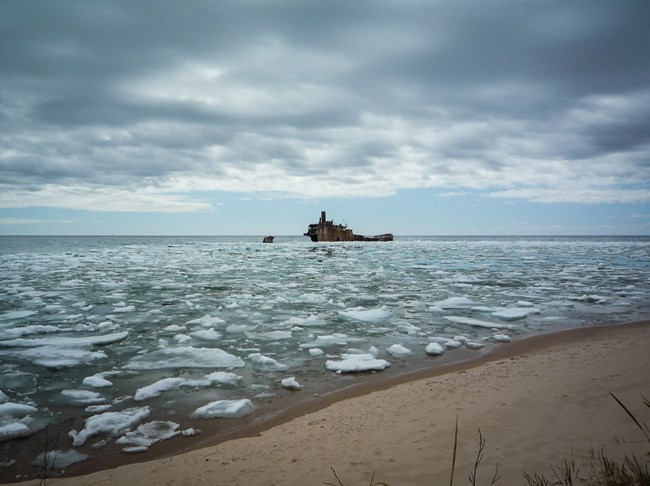 Part of a metal ship above water surrounded by ice chunks.