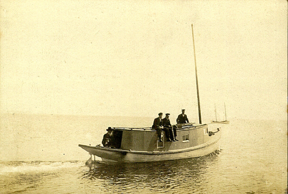 A small boat sails through calm water. Four people are visible on the boat.