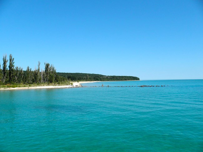 Island beach with old pilings sticking up from the blue-green water of Lake Michigan
