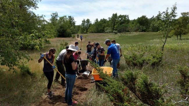 Kettles-Trail-Project People with shovels and a wheel barrel work on the dirt trail