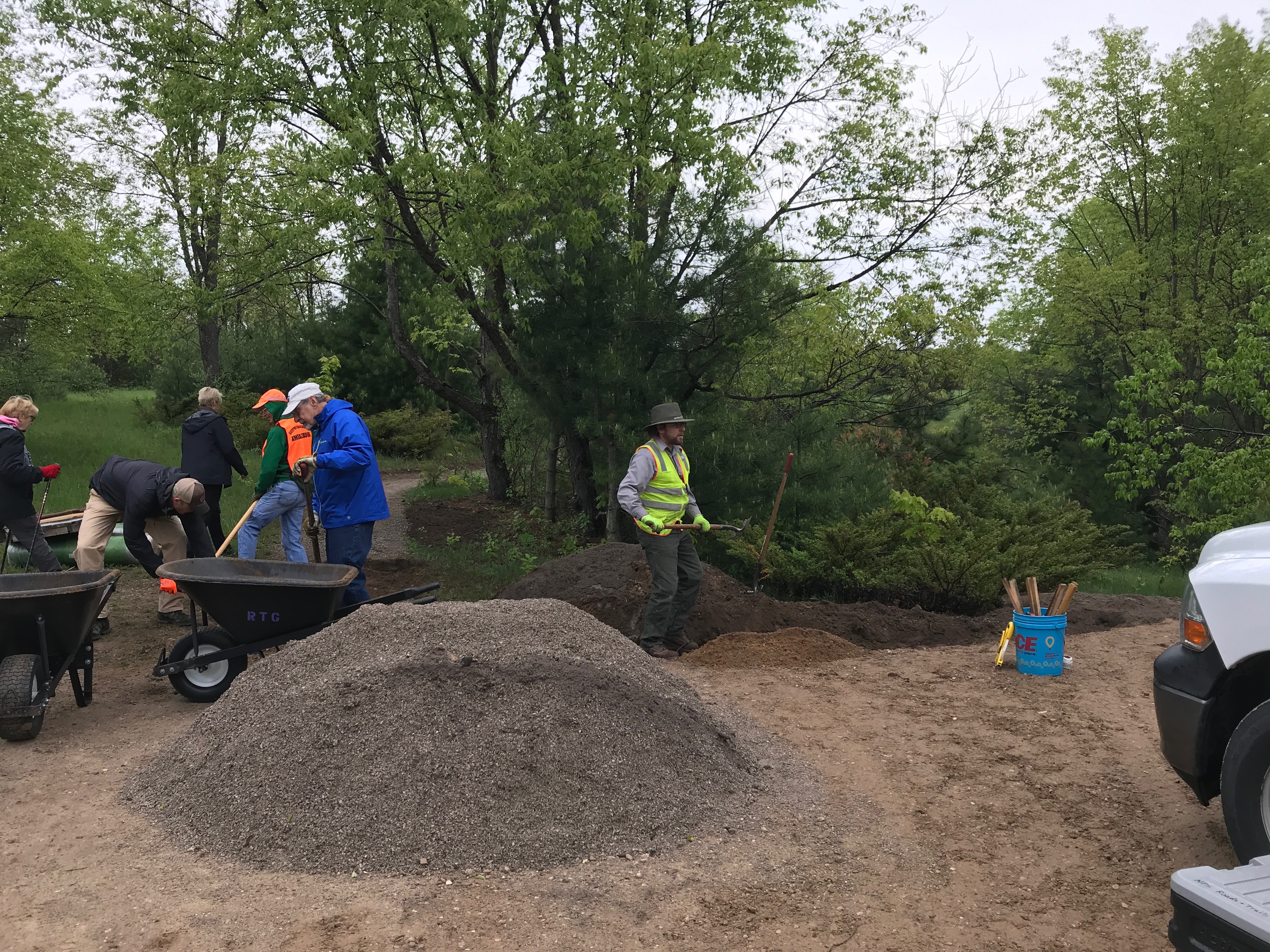 Volunteers using rakes and wheelbarrows add gravel to a trail