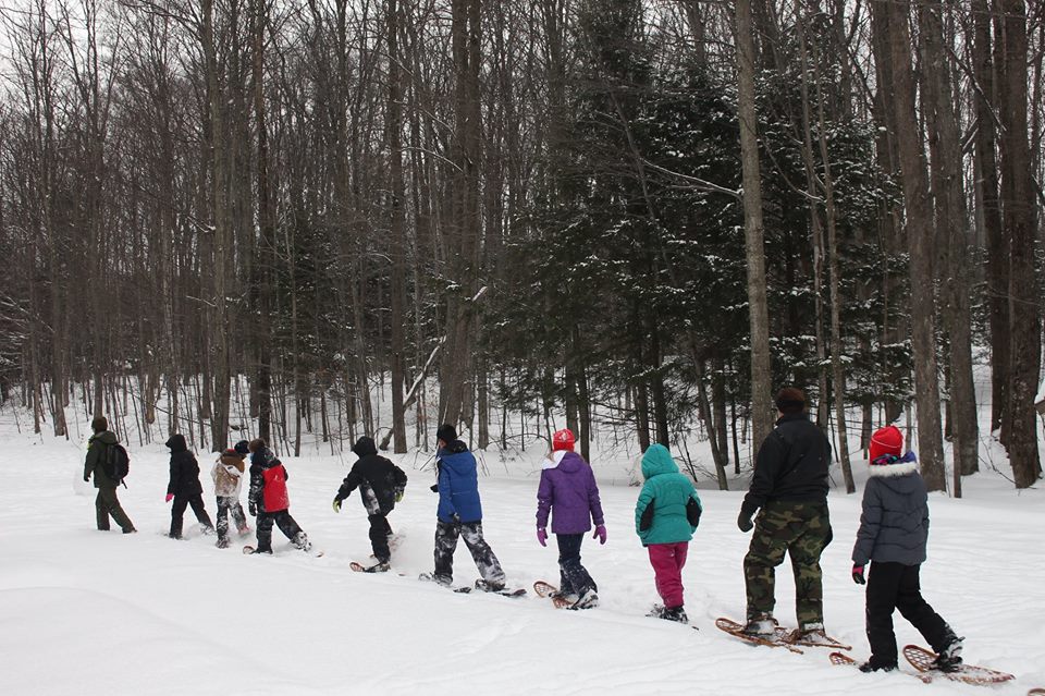 Snowshoe-Experience A row of winter-geared and snow-shoed school children follow a ranger on a snowshoe hike.
