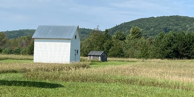 White outbuilding sits in green field with tree-covered ridges in background