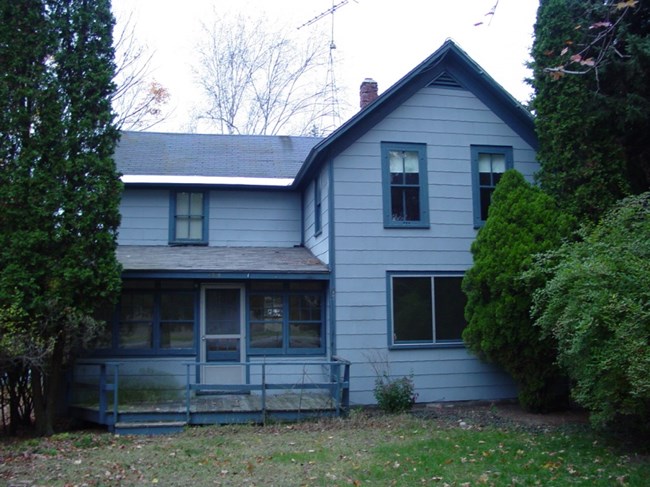 Blue farmhouse with darker blue trim and screened front porch