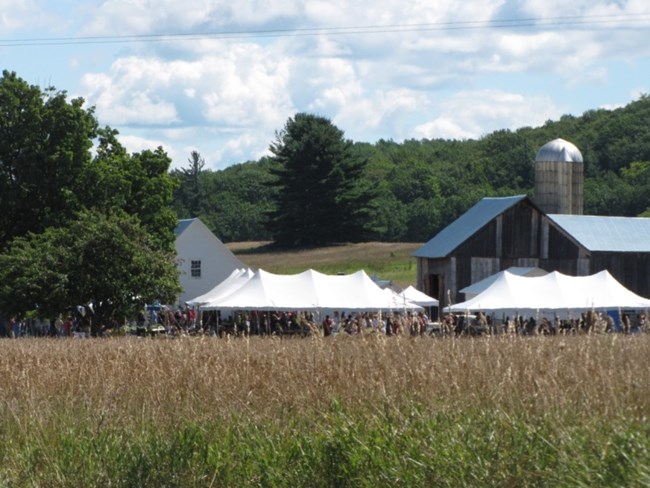 White tents in front of farm buildings with meadow in foreground