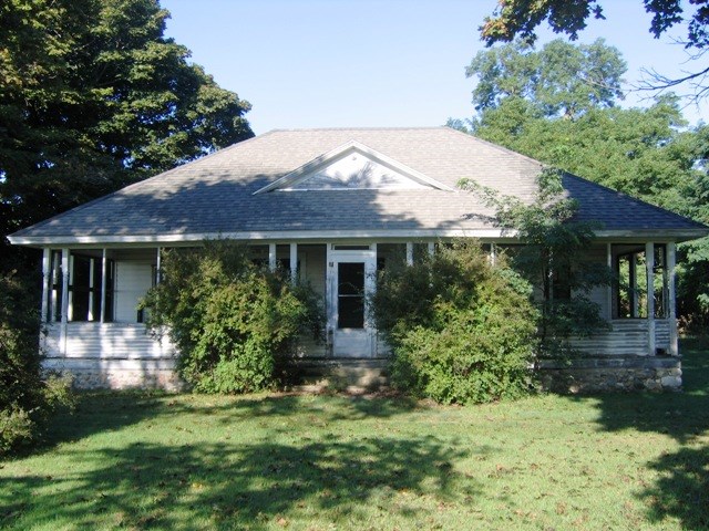 One-storied cottage with covered porch obscured by two large green bushes flanking the front door