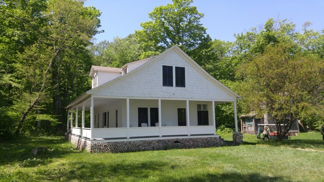 White cottage with dormers in roof, wrap around covered porch and small rock foundation