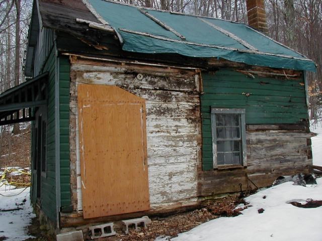 Weathered cabin with tarp on roof and side porch removed