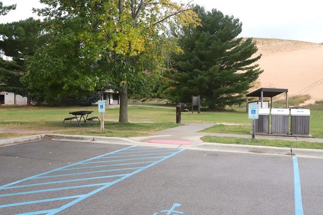 Handicapped-accessible parking spaces in front of a flat grassy area backed by a large sand dune.