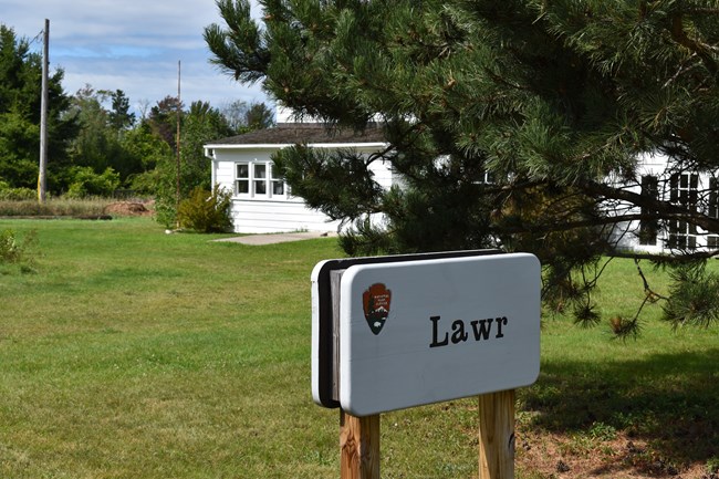 A sign the says Lawr stands in front of a farmhouse.