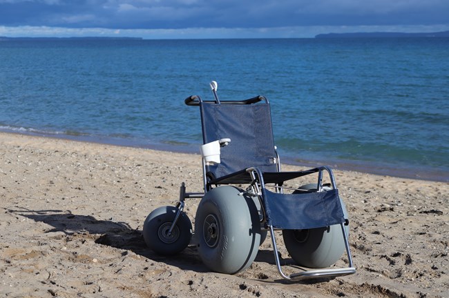 A blue wheelchair with oversize inflatable wheels sits on a beach in front of blue water.